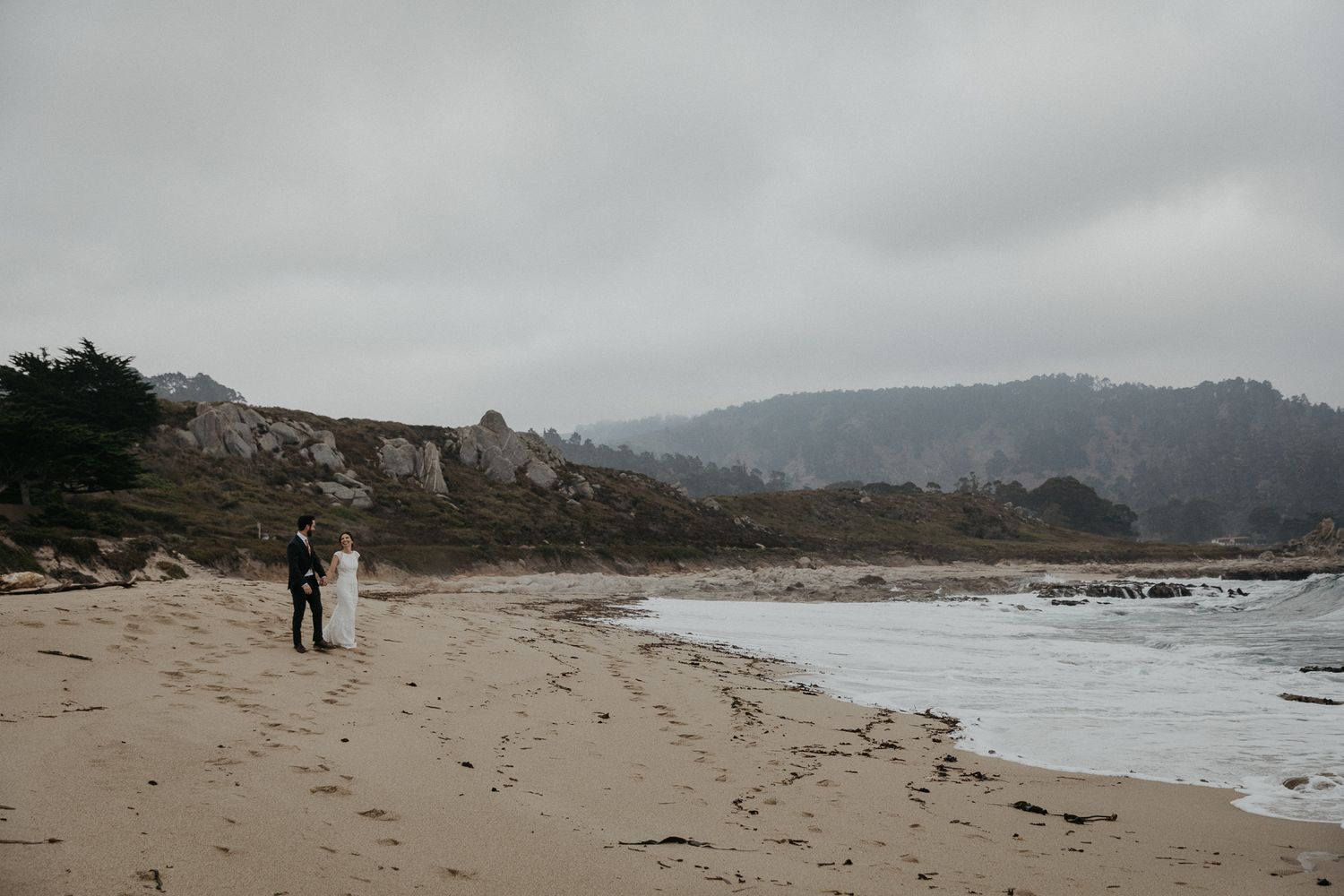 A distant view of a coastal wedding ceremony with cliffs and ocean waves in the background.