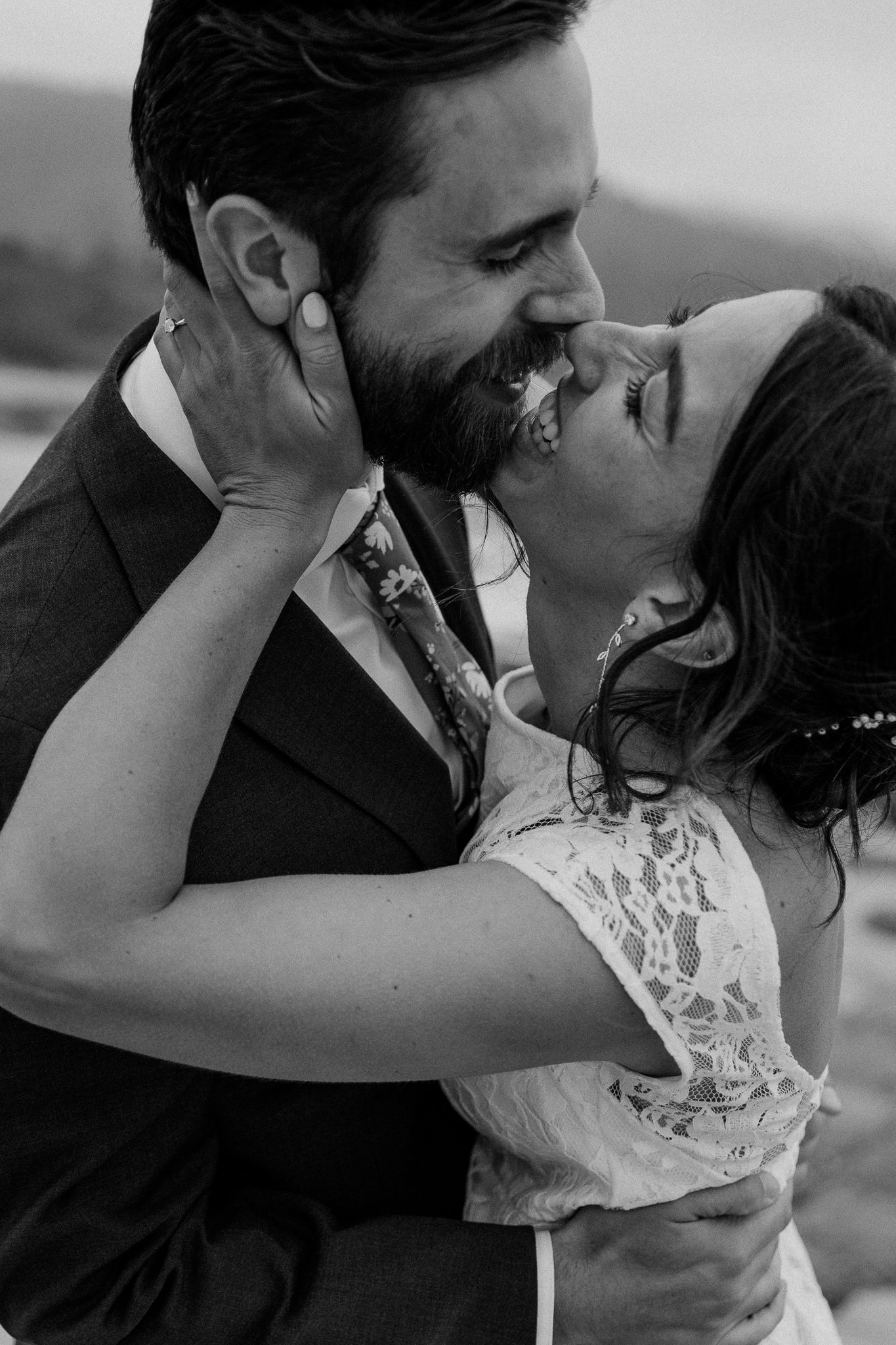 An intimate black and white wedding portrait shows a couple sharing a passionate moment on the beach.