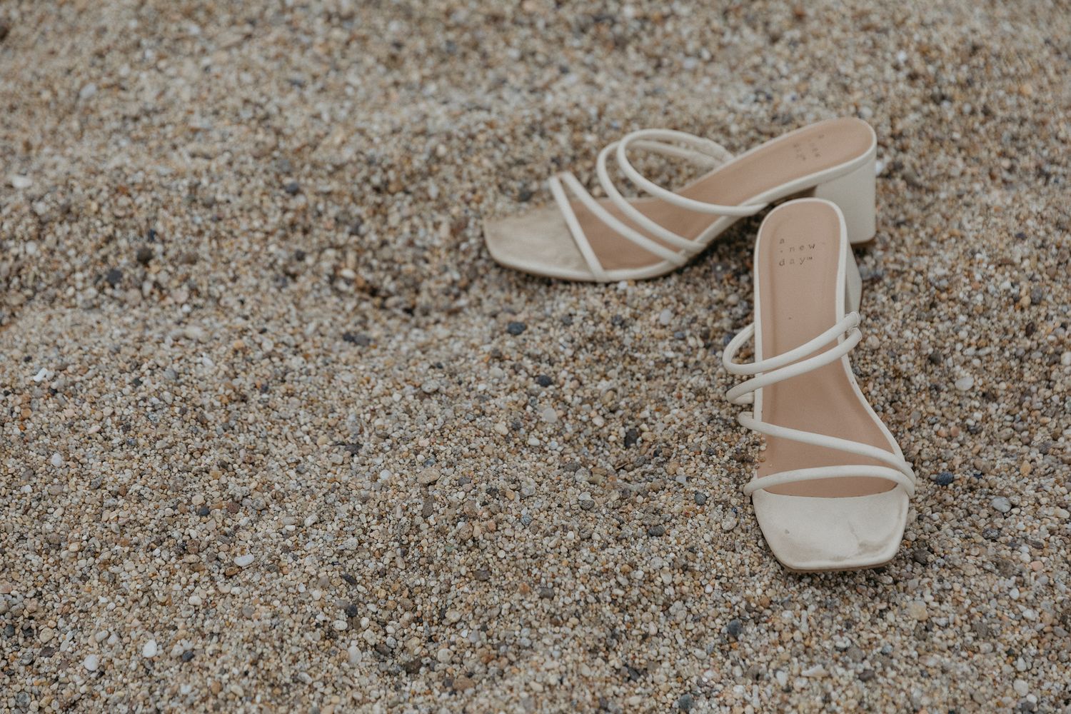 A pair of elegant beige strappy wedding sandals placed on sandy ground.
