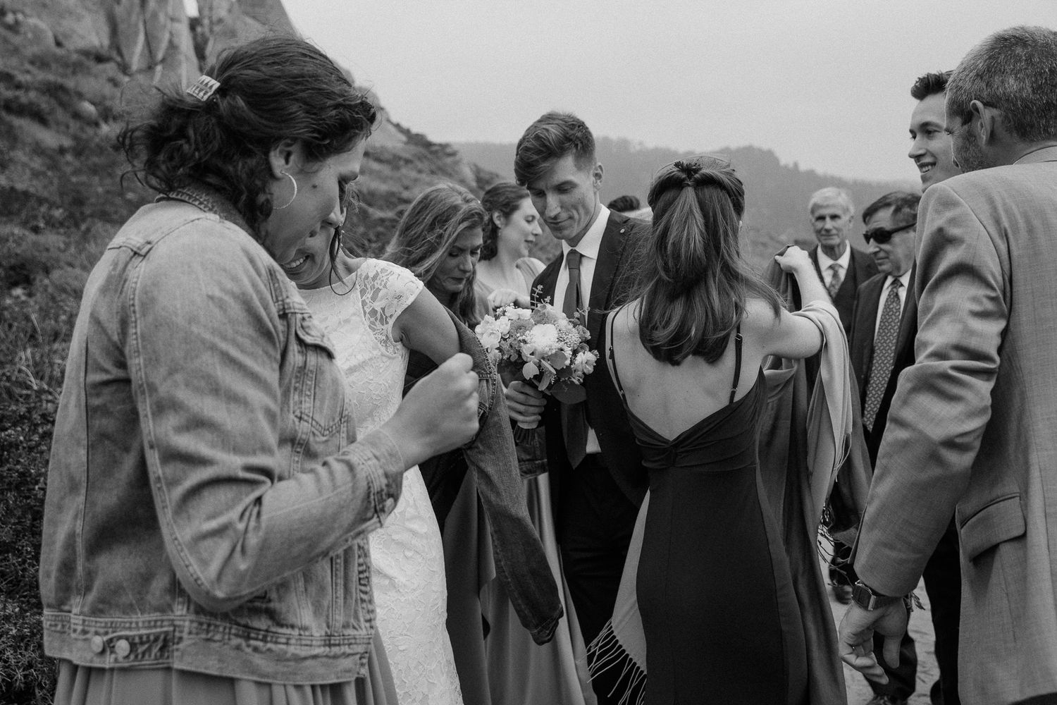 Wedding guests gather outdoors during a casual celebration with one person wearing a denim jacket.
