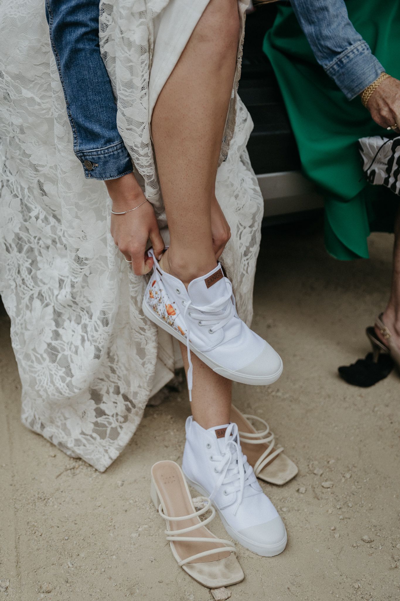 Close-up of someone changing into white sneakers while wearing a wedding dress.