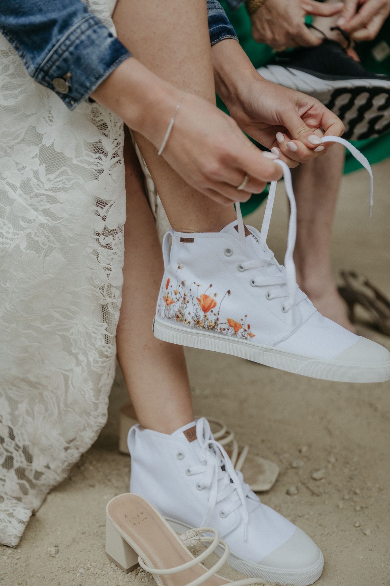 Detail shot of white floral-decorated sneakers being laced up with wedding dress fabric visible.
