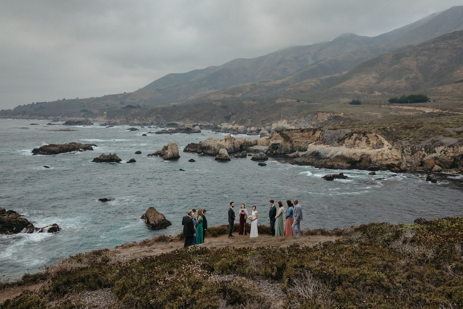 Aerial view of wedding party gathered on dramatic Big Sur coastline.