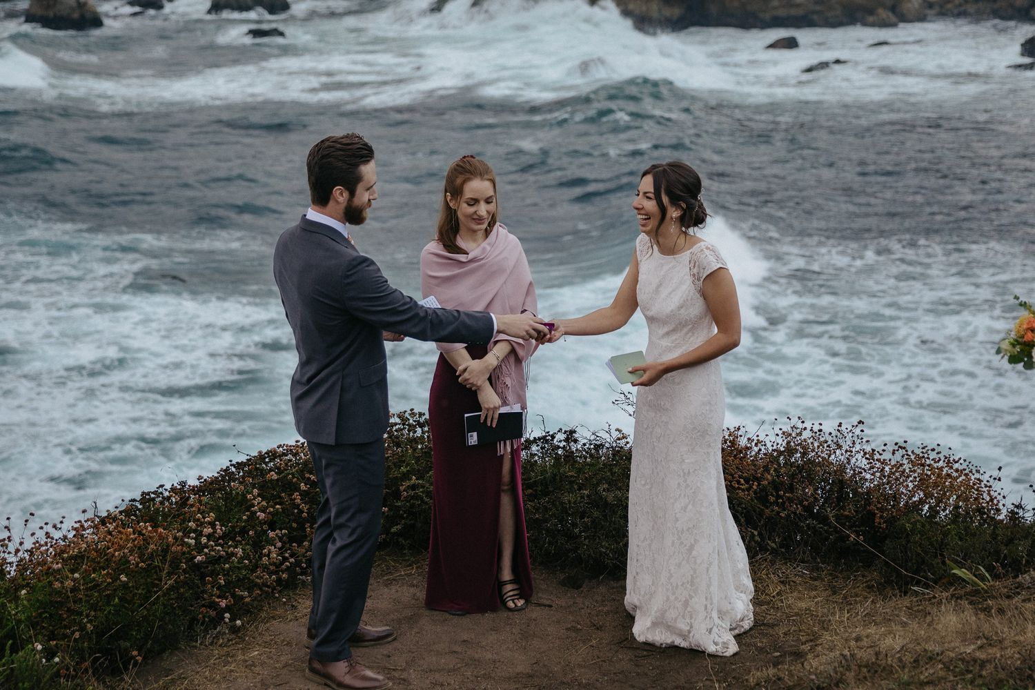 A wedding officiant conducts a ceremony on a cliff with crashing waves below.