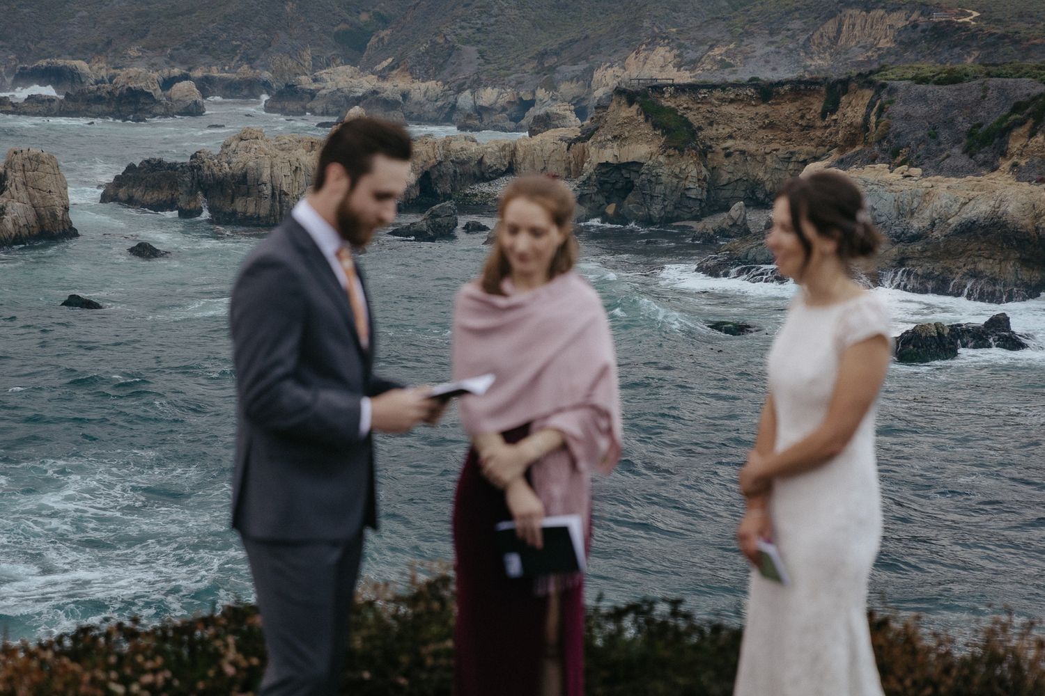 An intimate wedding ceremony takes place against a dramatic rocky coastline.