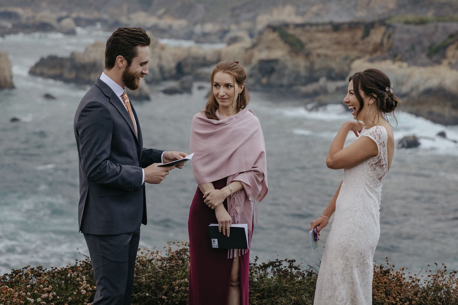 A wedding ceremony unfolds on a cliff with waves crashing on rocks below.