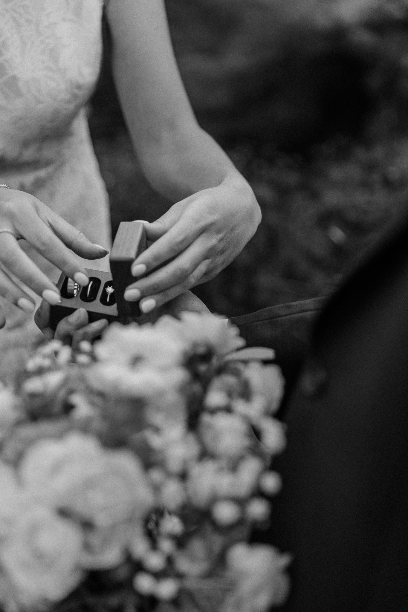 Closeup of hands holding a ring with floral bouquet in black and white.