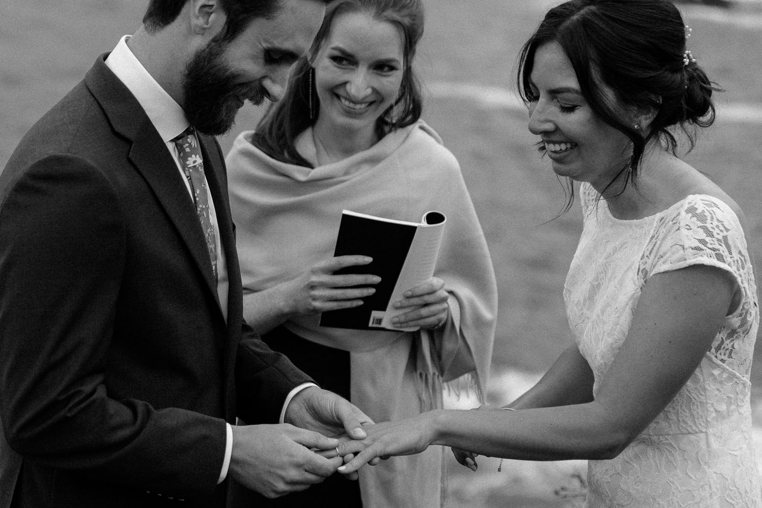 Intimate wedding ceremony moment with officiant and couple exchanging rings outdoors.