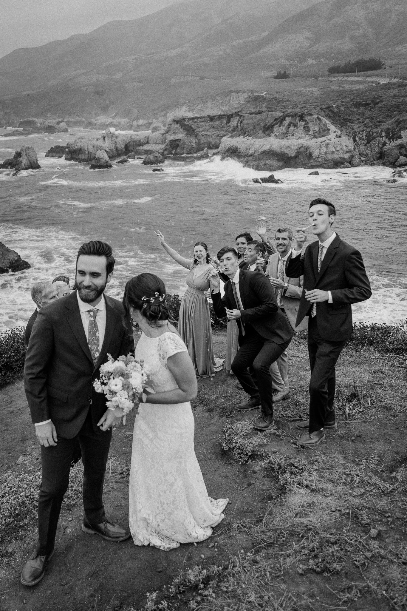Wedding party poses on dramatic coastal cliffs overlooking a rugged ocean shoreline.