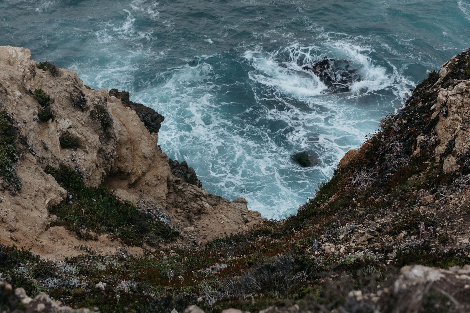 Dramatic aerial view of turquoise ocean waves crashing against rocky coastal cliffs.