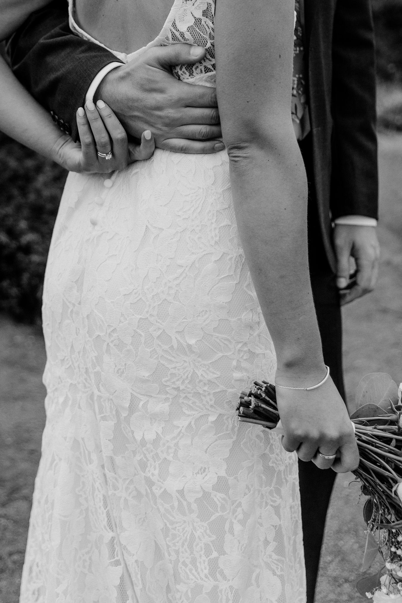 Close-up detail of lace wedding dress and gentle embrace in black and white.