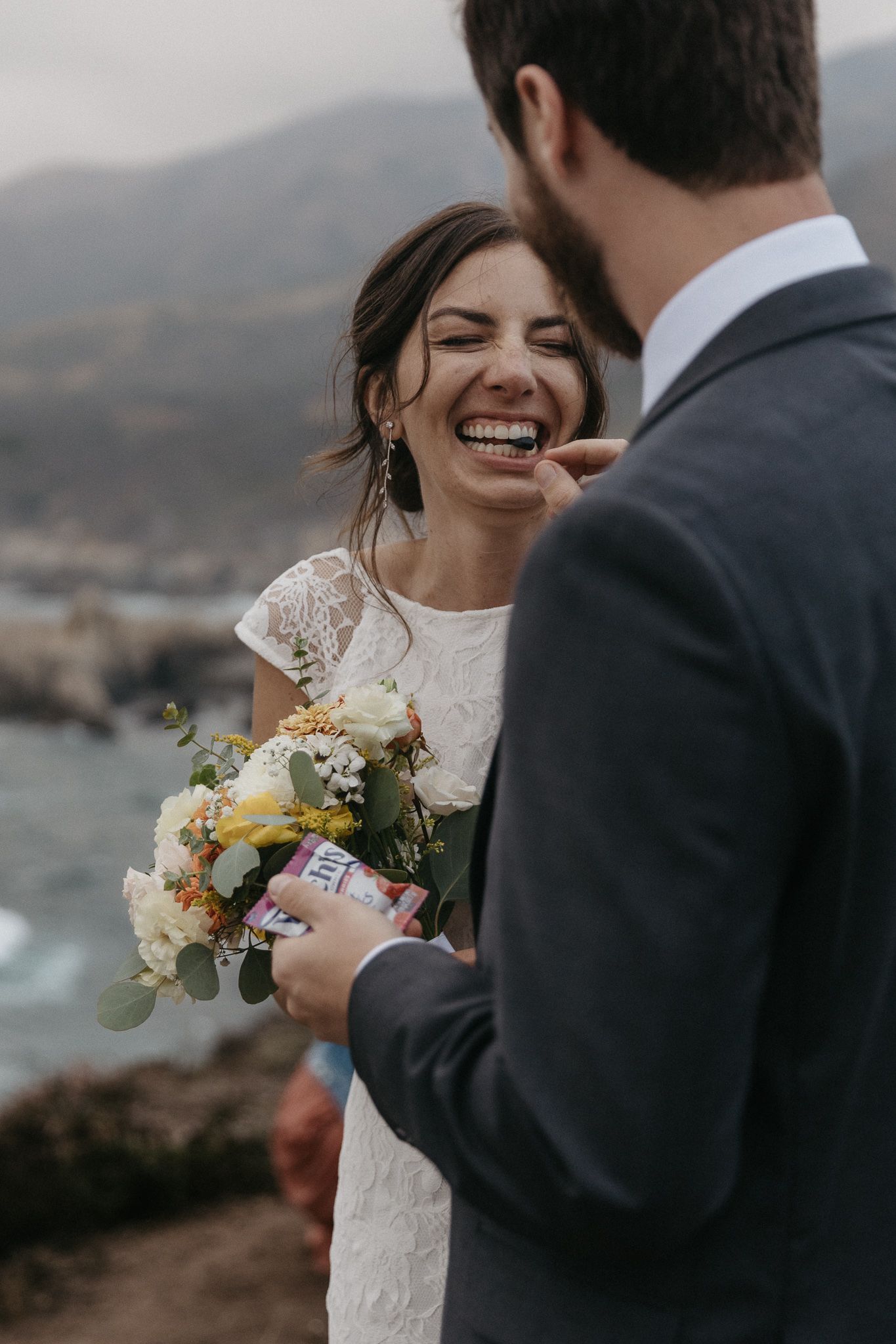 Joyful wedding couple sharing a moment on a scenic coastal cliff.