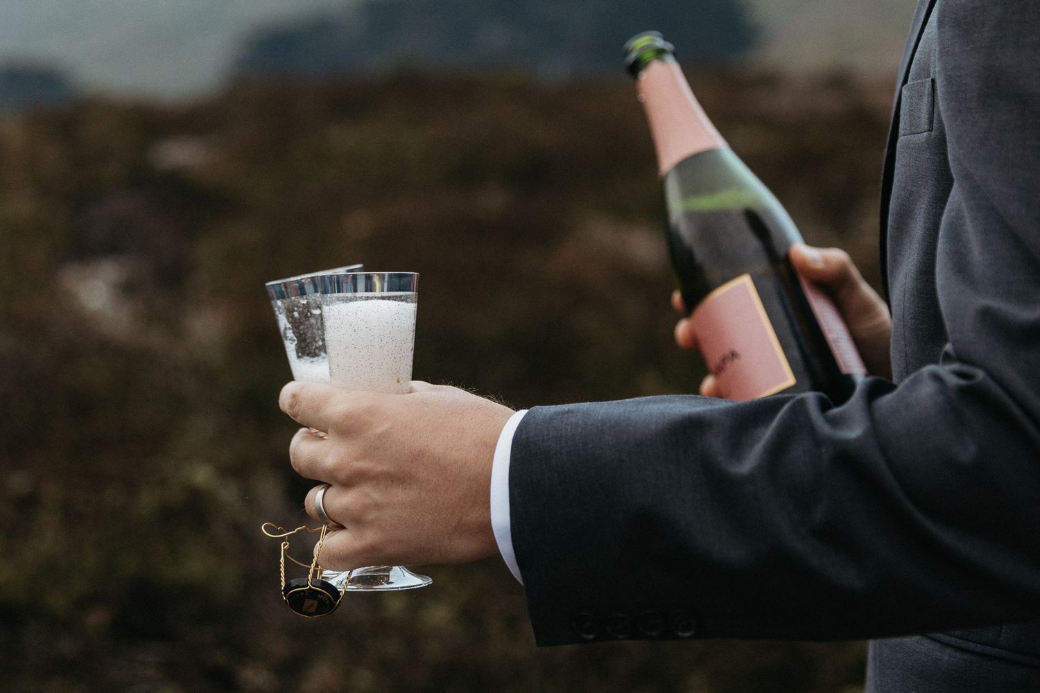 Close-up of hands pouring champagne into glass with coastal scenery in background.