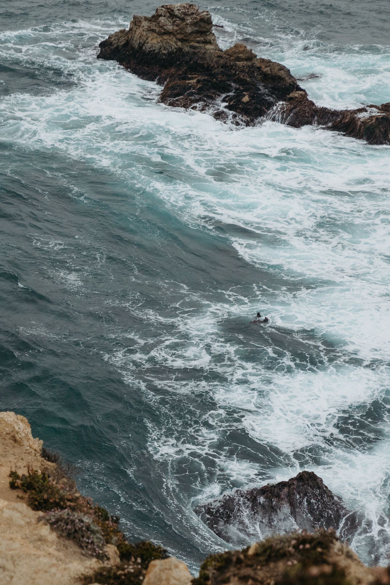 Dramatic coastal scene with waves crashing against rocky cliffs in stormy weather.