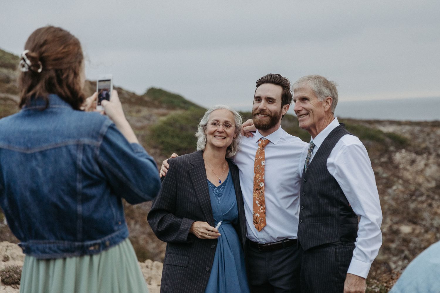 A photographer captures a group photo at an outdoor celebration near the coast.