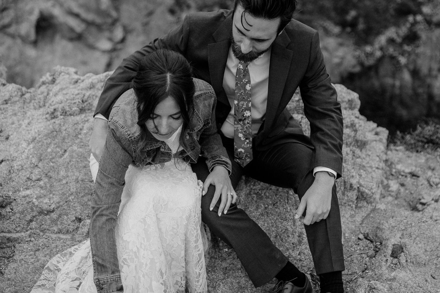 A wedding couple shares a tender moment on rocky terrain in black and white.