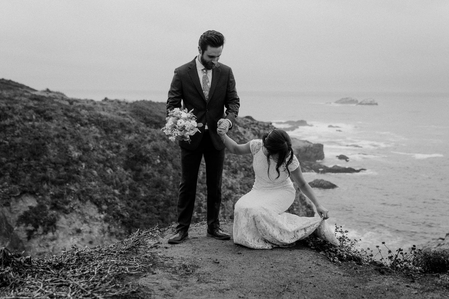 A couple shares an intimate moment on a cliff edge overlooking the Pacific coast.