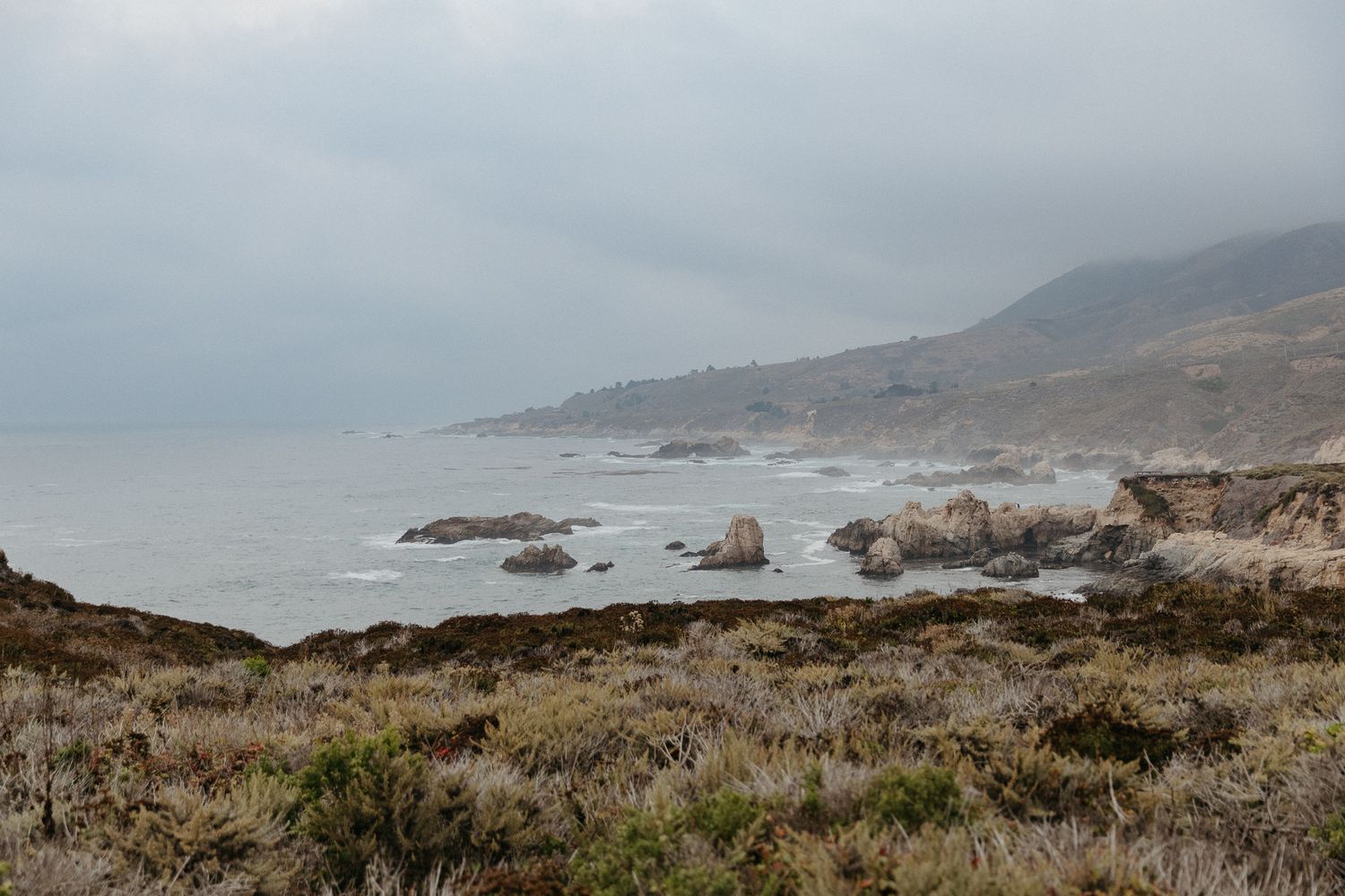 Dramatic coastal landscape with rocky cliffs and misty shoreline along Big Sur's rugged California coastline.