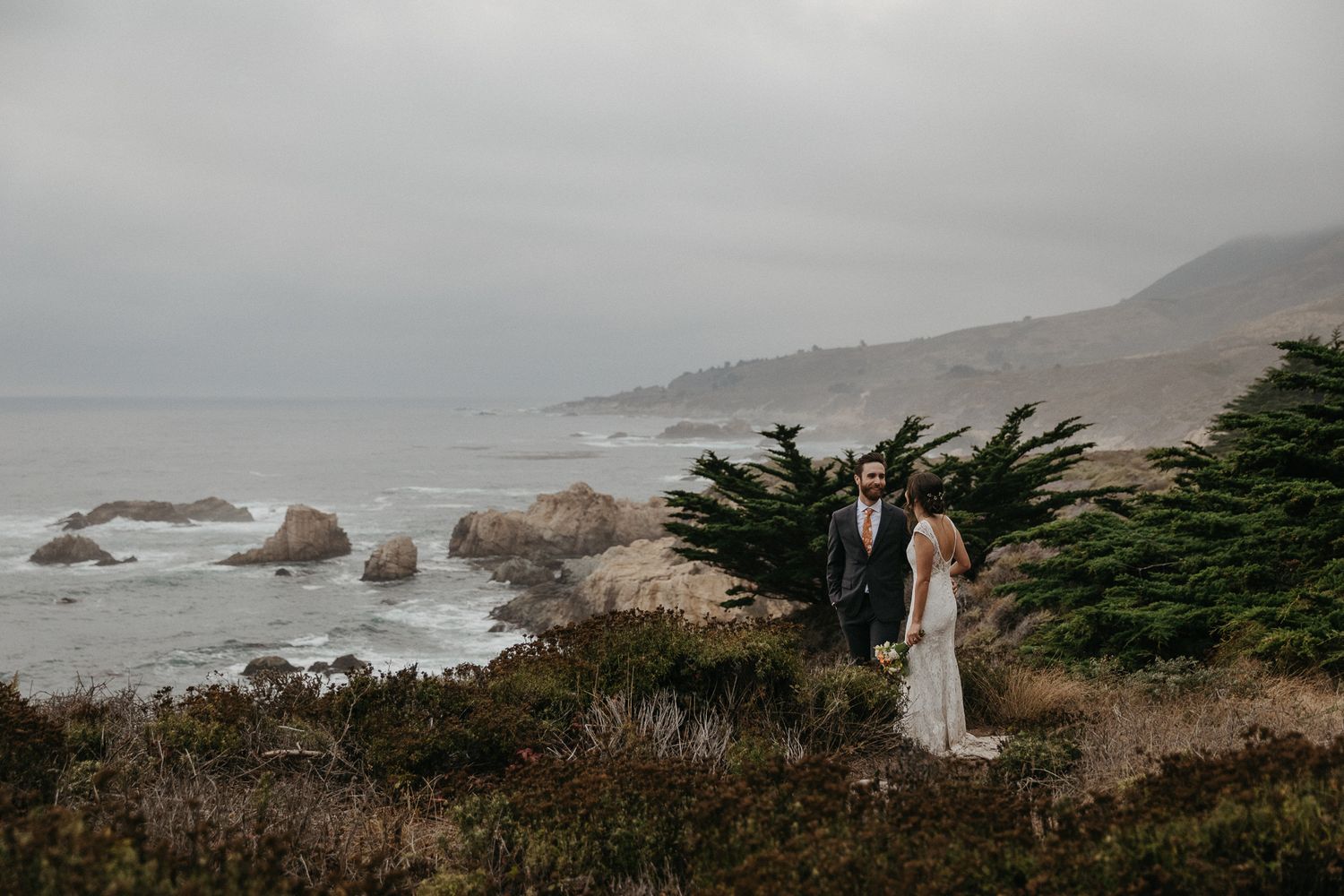 A misty coastal wedding photo with cliffside views of the Pacific Ocean and cypress trees.