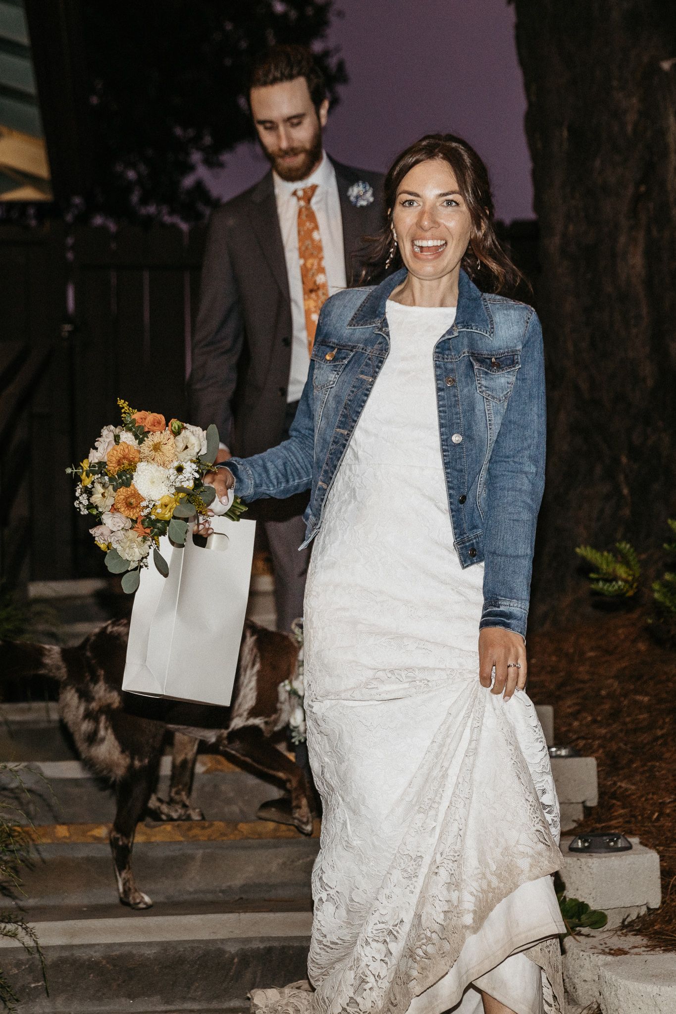 A wedding couple with their Australian Shepherd dog on steps at dusk.