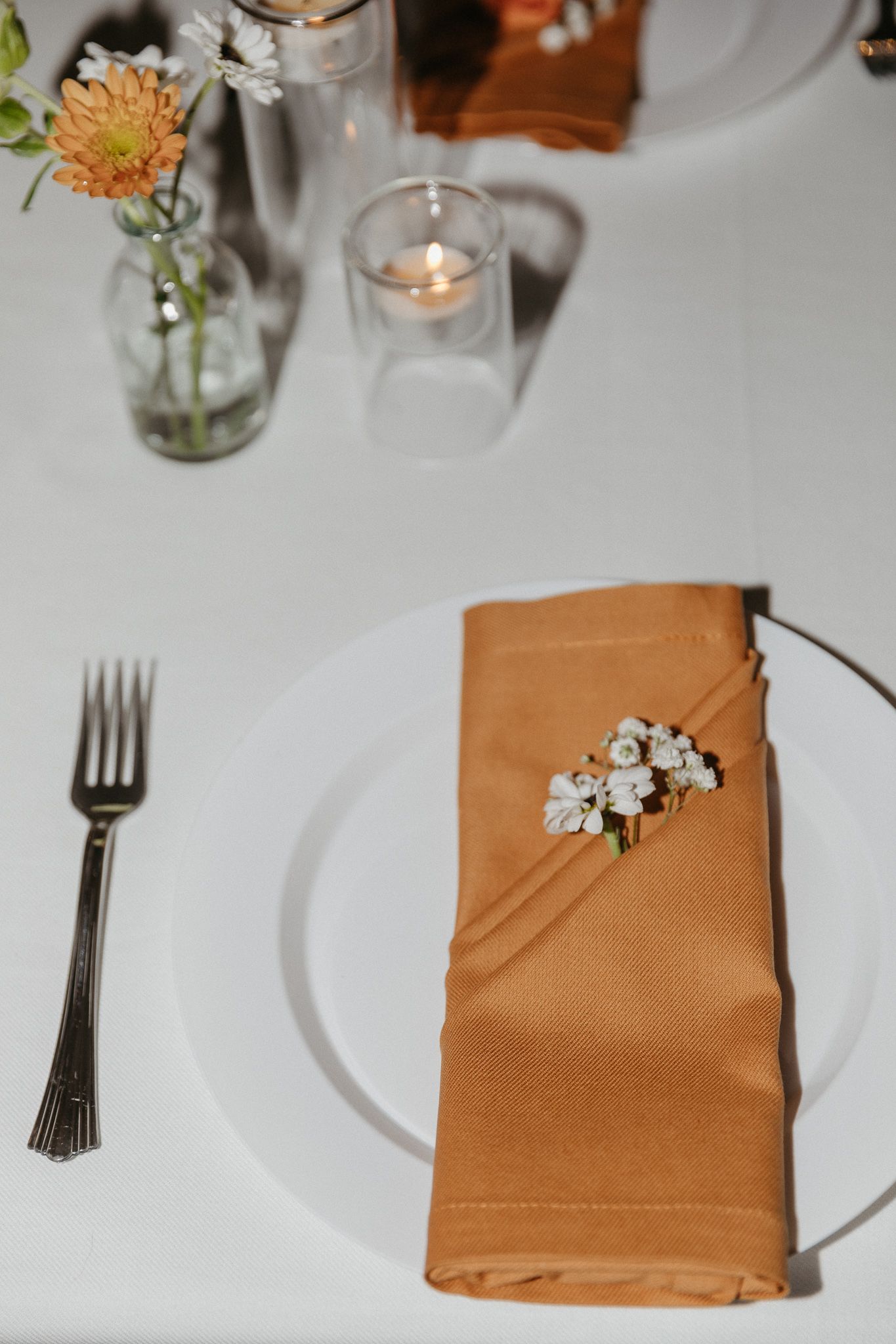 Wedding place setting with orange napkin, white plate, and floral accent.