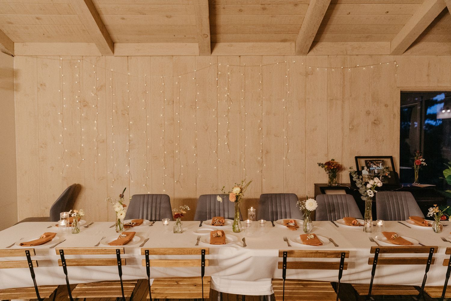 Long wooden wedding reception table set with white linens and natural decor.