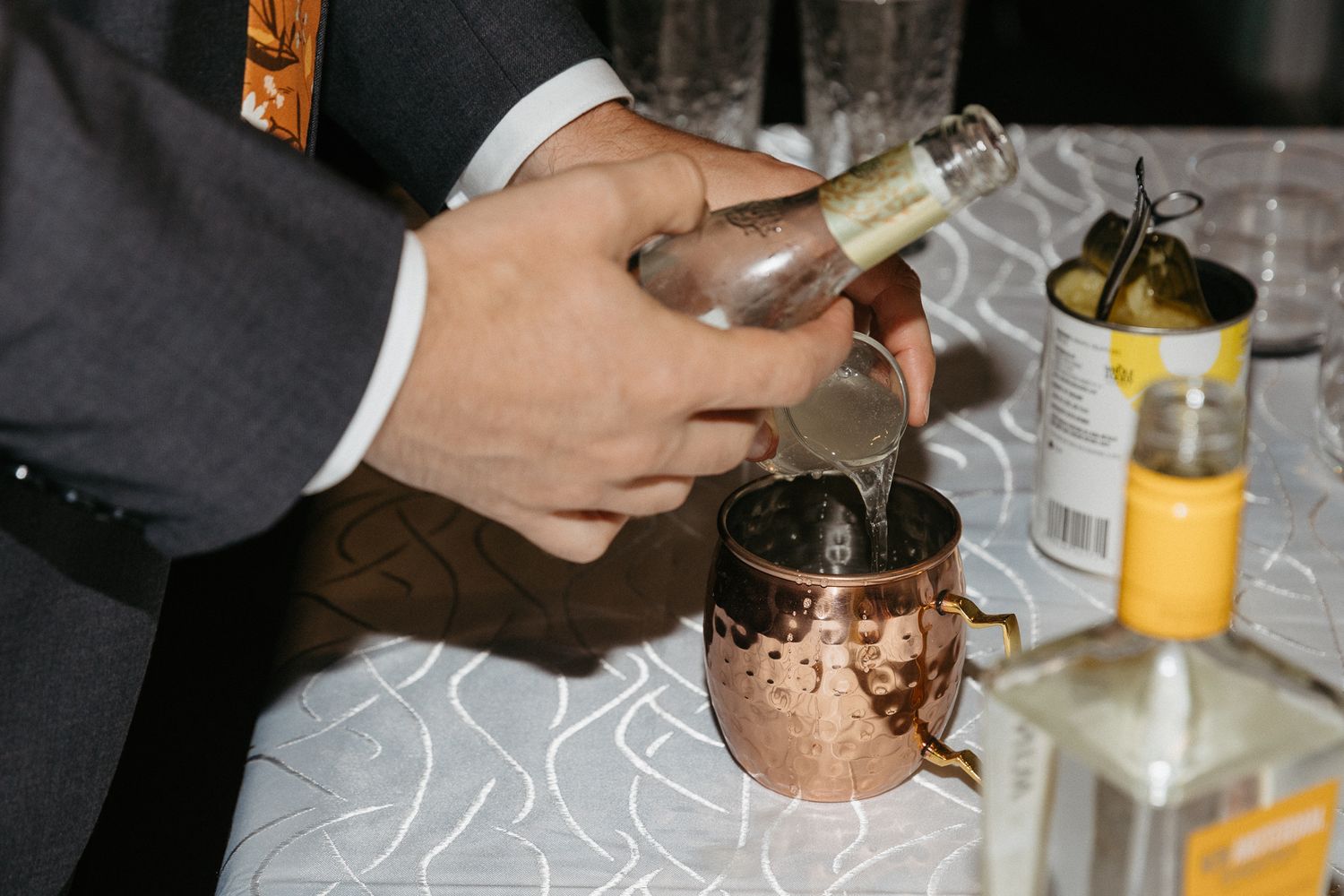 Hands pouring a cocktail into copper mug at wedding reception.