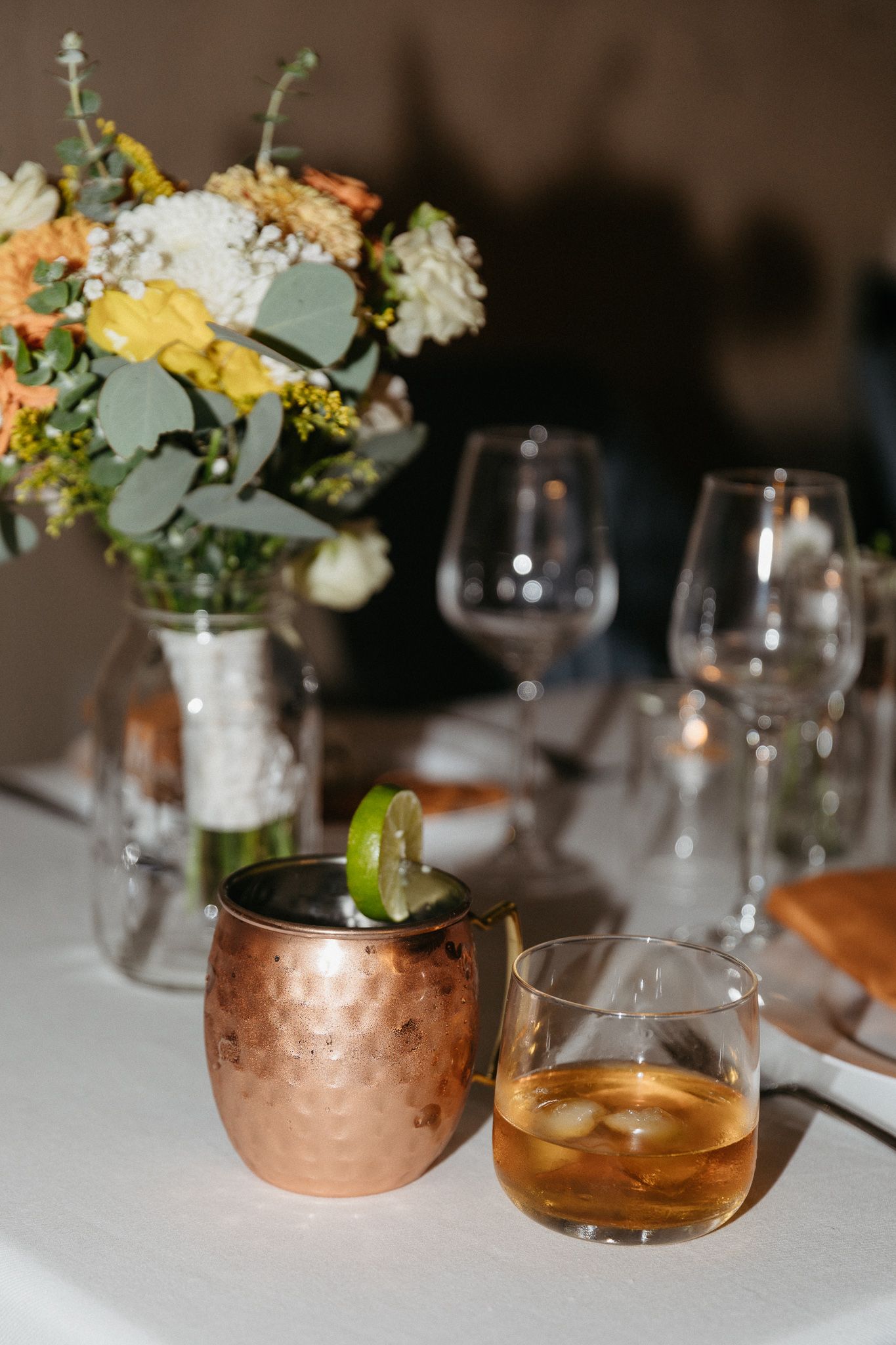 Elegant cocktails and floral centerpiece on white tablecloth at wedding reception.