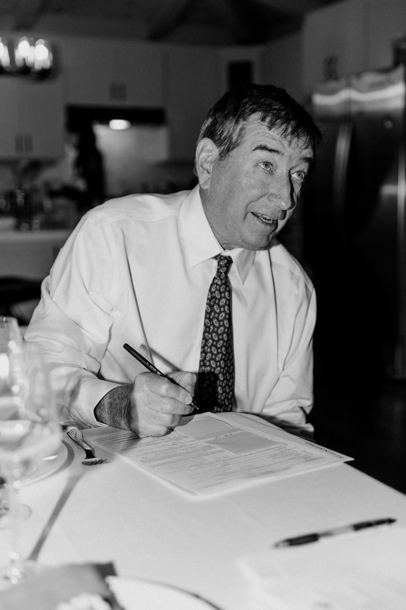 Black and white portrait of guest signing document at formal event.