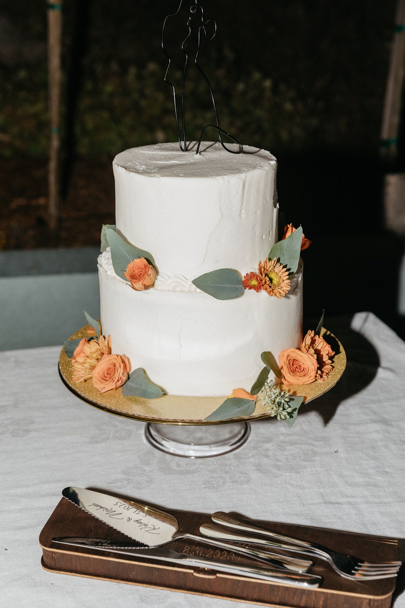 White two-tier wedding cake decorated with peach flowers and eucalyptus leaves.