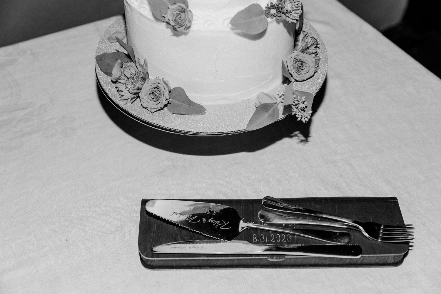 Black and white close-up of wedding cake cutting set on dark surface.