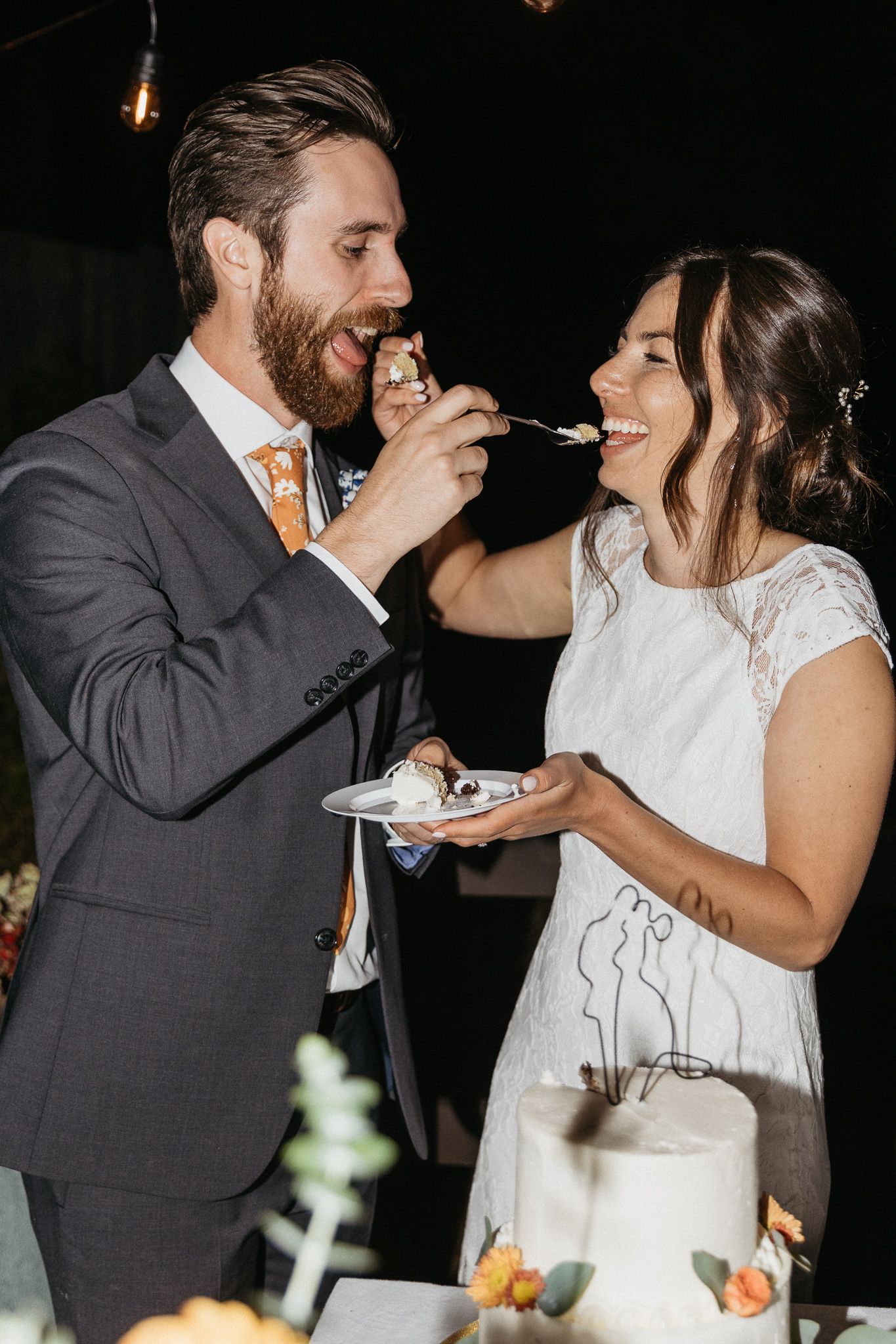 A couple playfully feeds each other bites of wedding cake during their reception celebration.