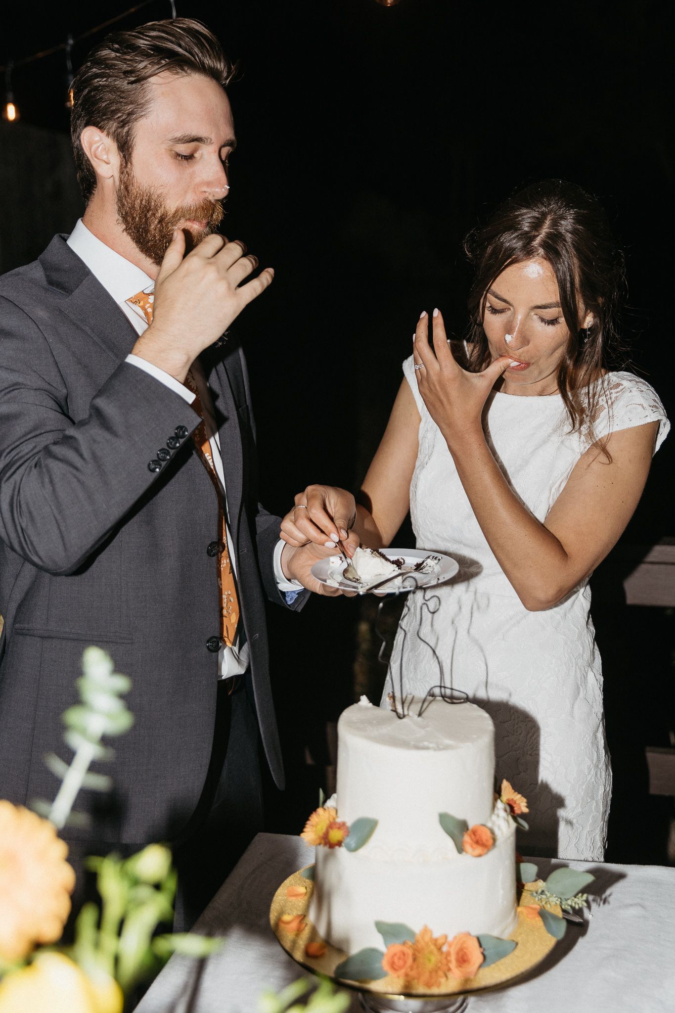 A couple enjoys their first bite of wedding cake together with playful expressions.