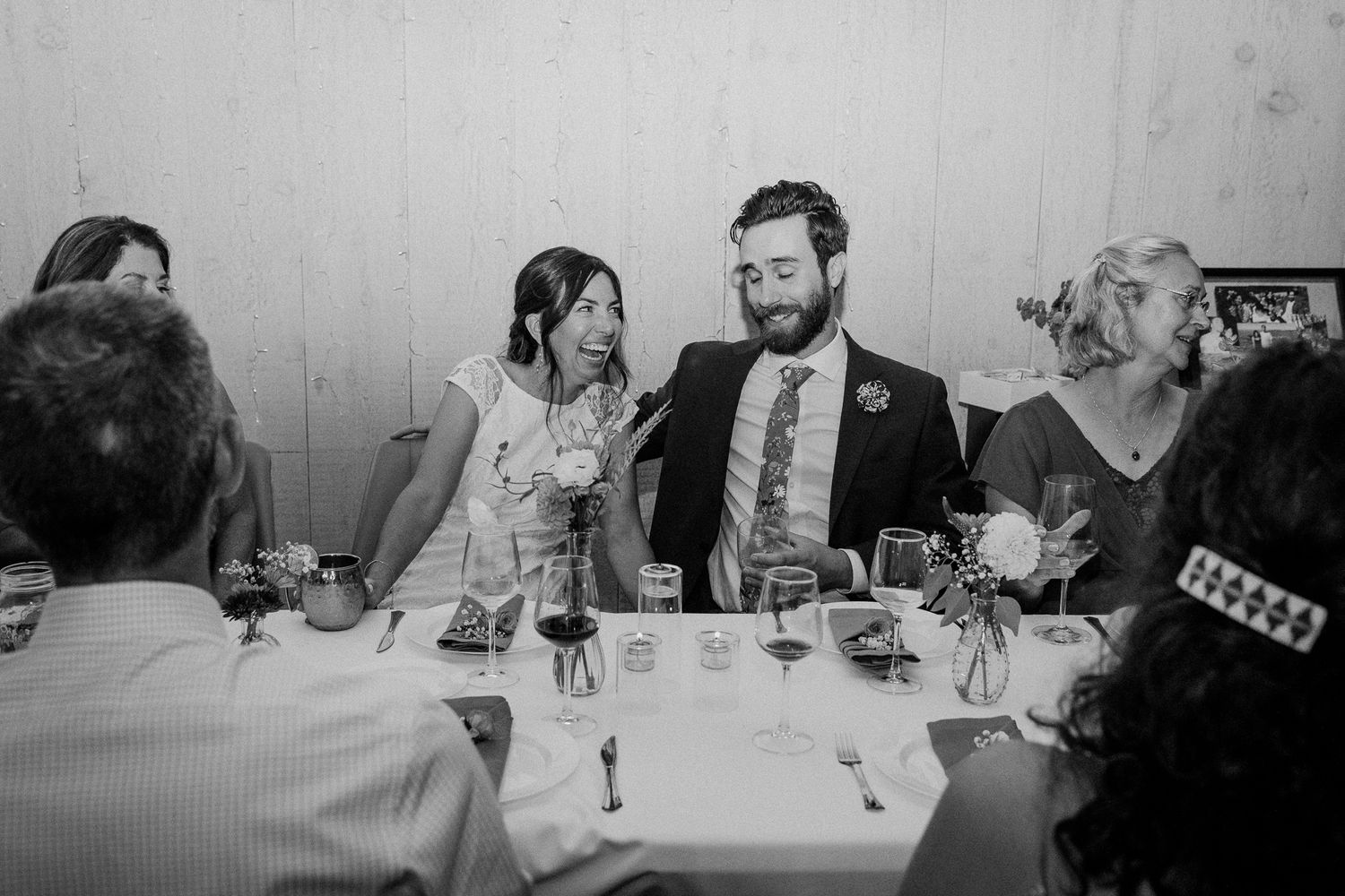 Wedding guests share laughs during dinner at a reception table setting.