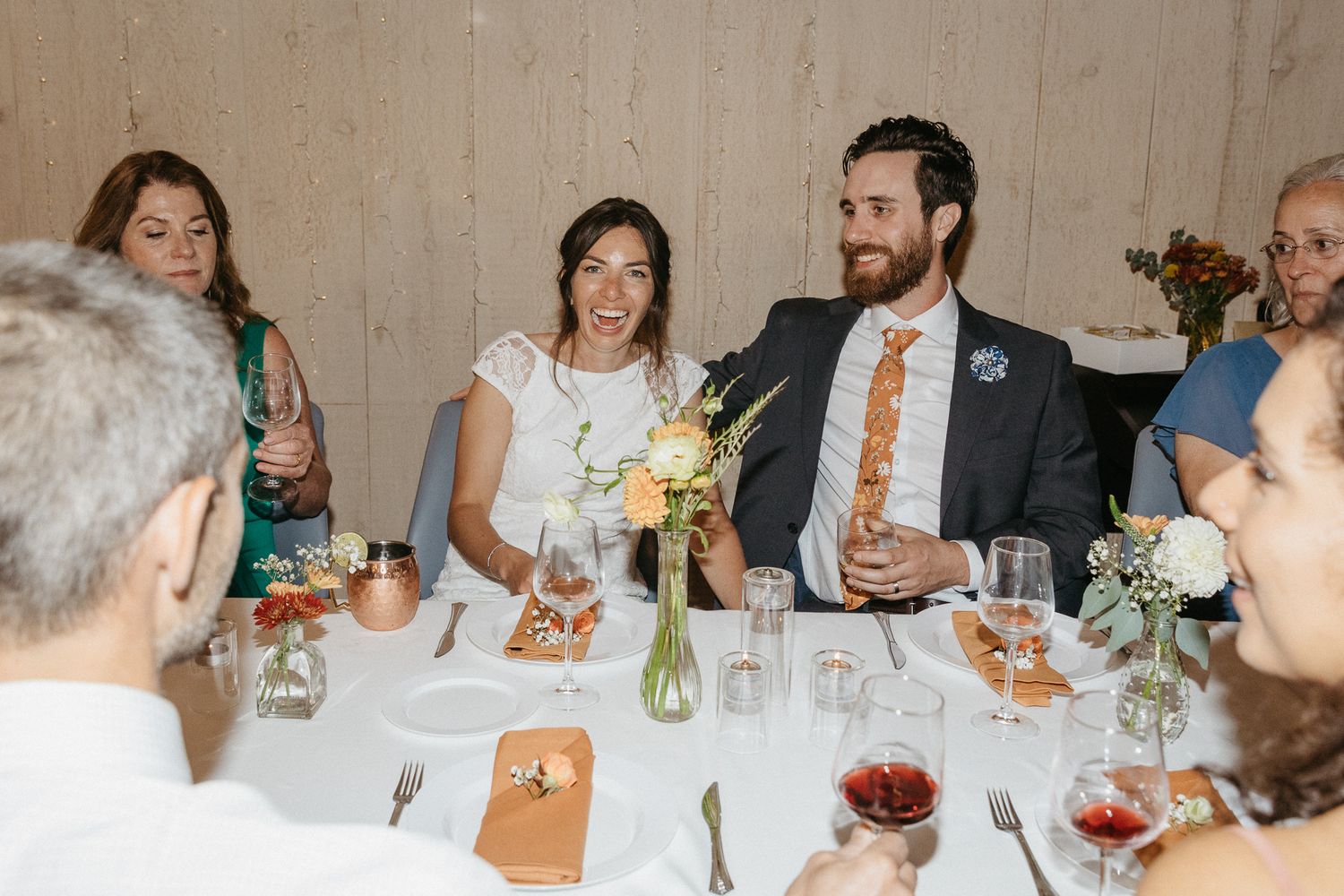 Reception guests enjoy dinner and drinks at an elegantly set table with floral centerpieces.