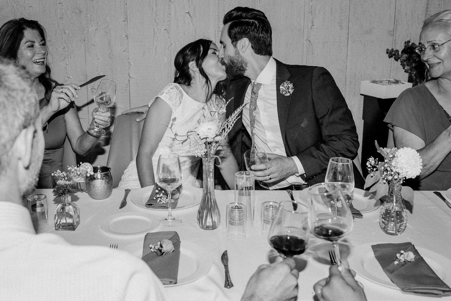 Black and white photo of wedding reception guests celebrating at an intimate dinner table.