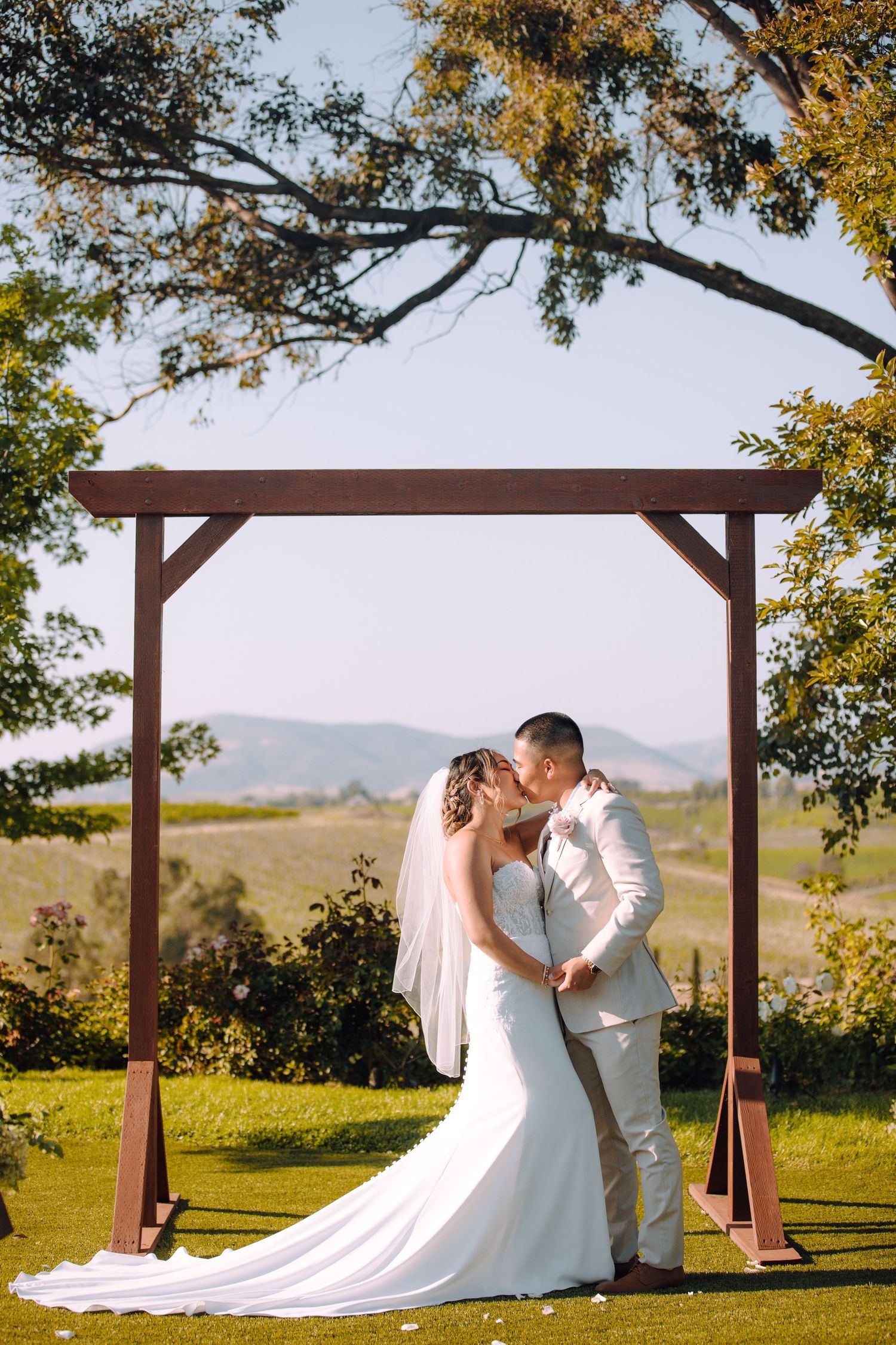A wedding ceremony under a wooden arch with mountain views in the background.