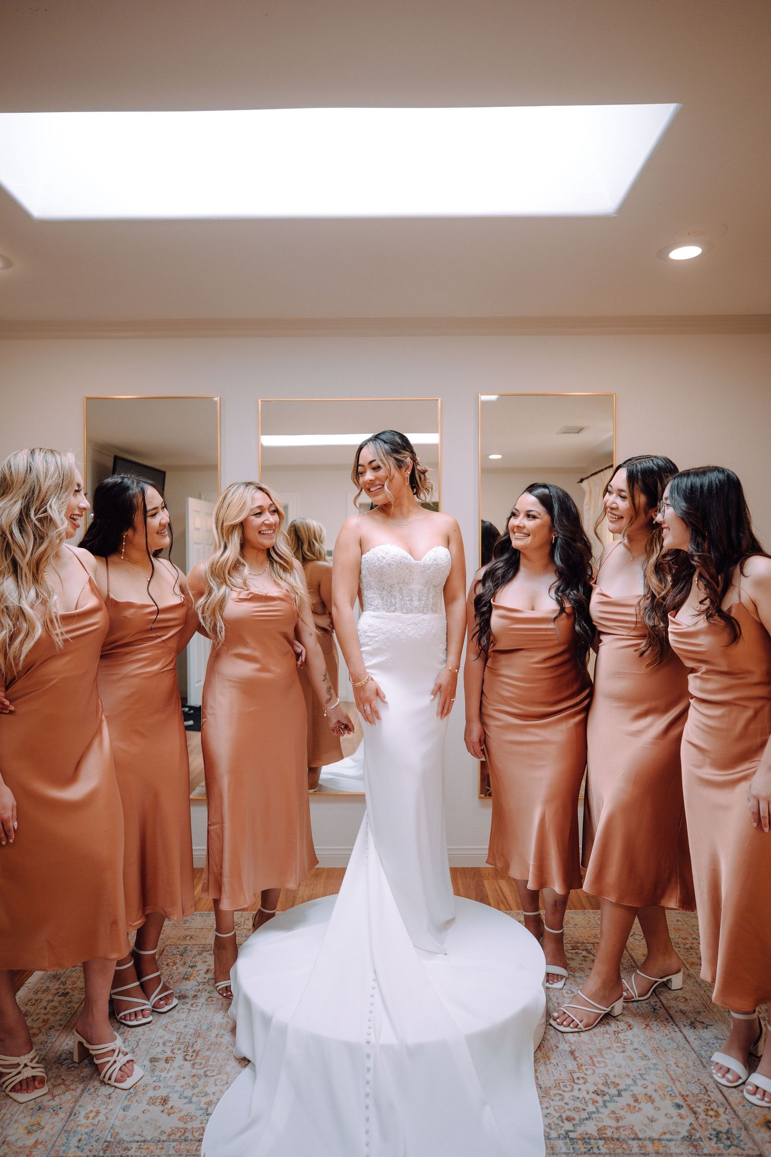 Bridesmaids in satin copper dresses surround a bride in white on her wedding day.