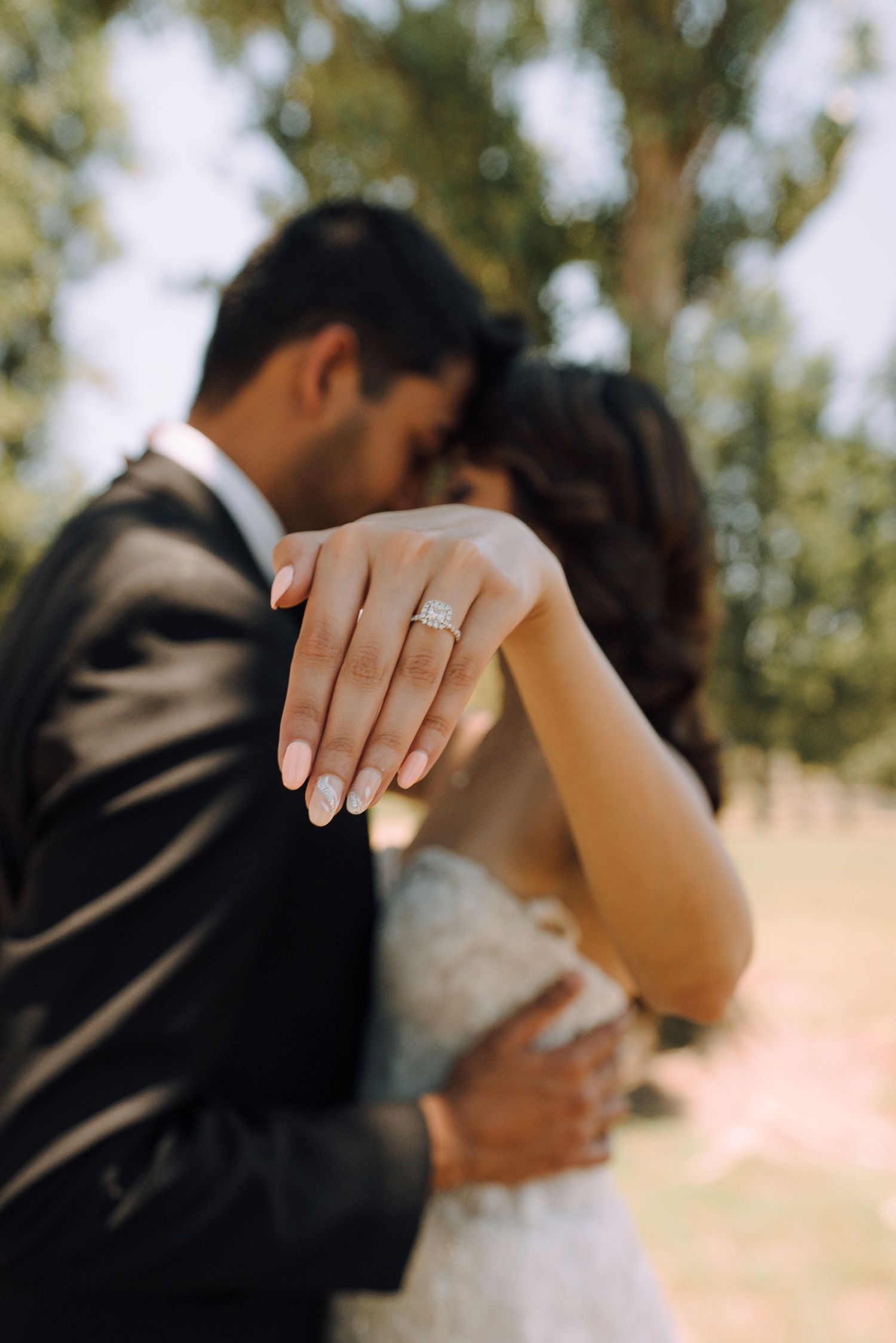 Close-up of bride showing engagement ring while embracing groom outdoors.