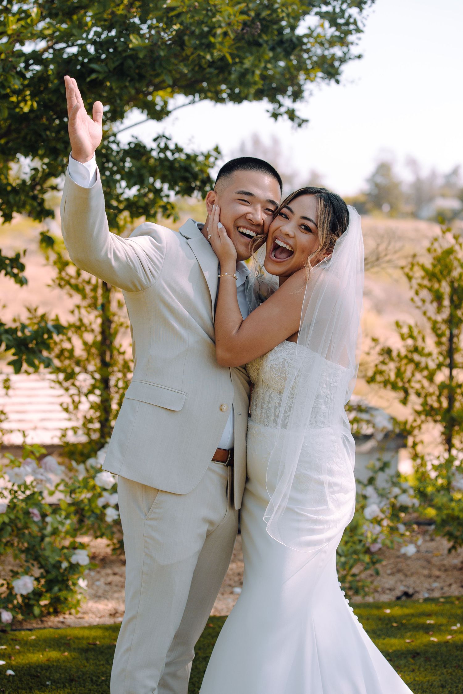 A joyful wedding couple celebrates in their white attire outdoors.