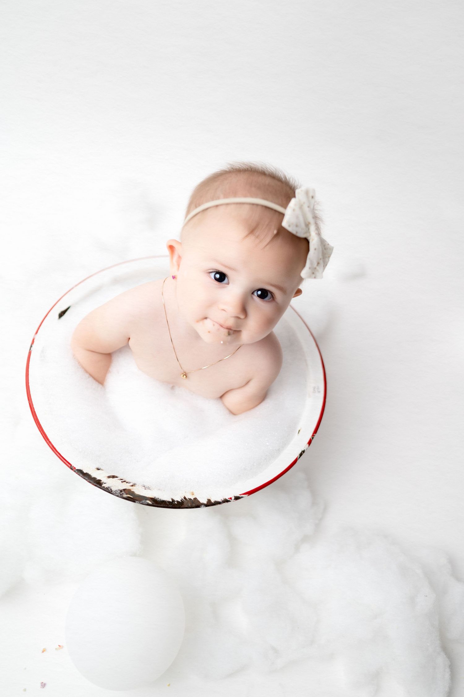 Baby sits in vintage white enamel bowl for milestone portrait session.