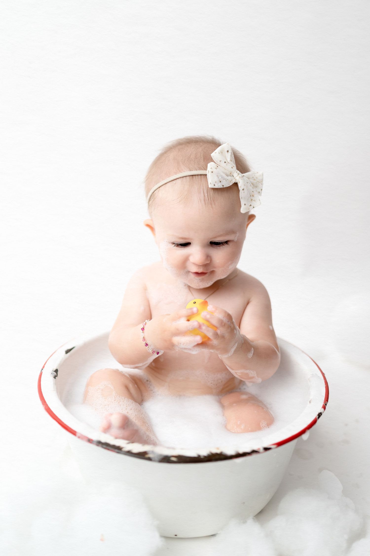 Baby plays with toy while sitting in vintage enamel bowl during portrait session.