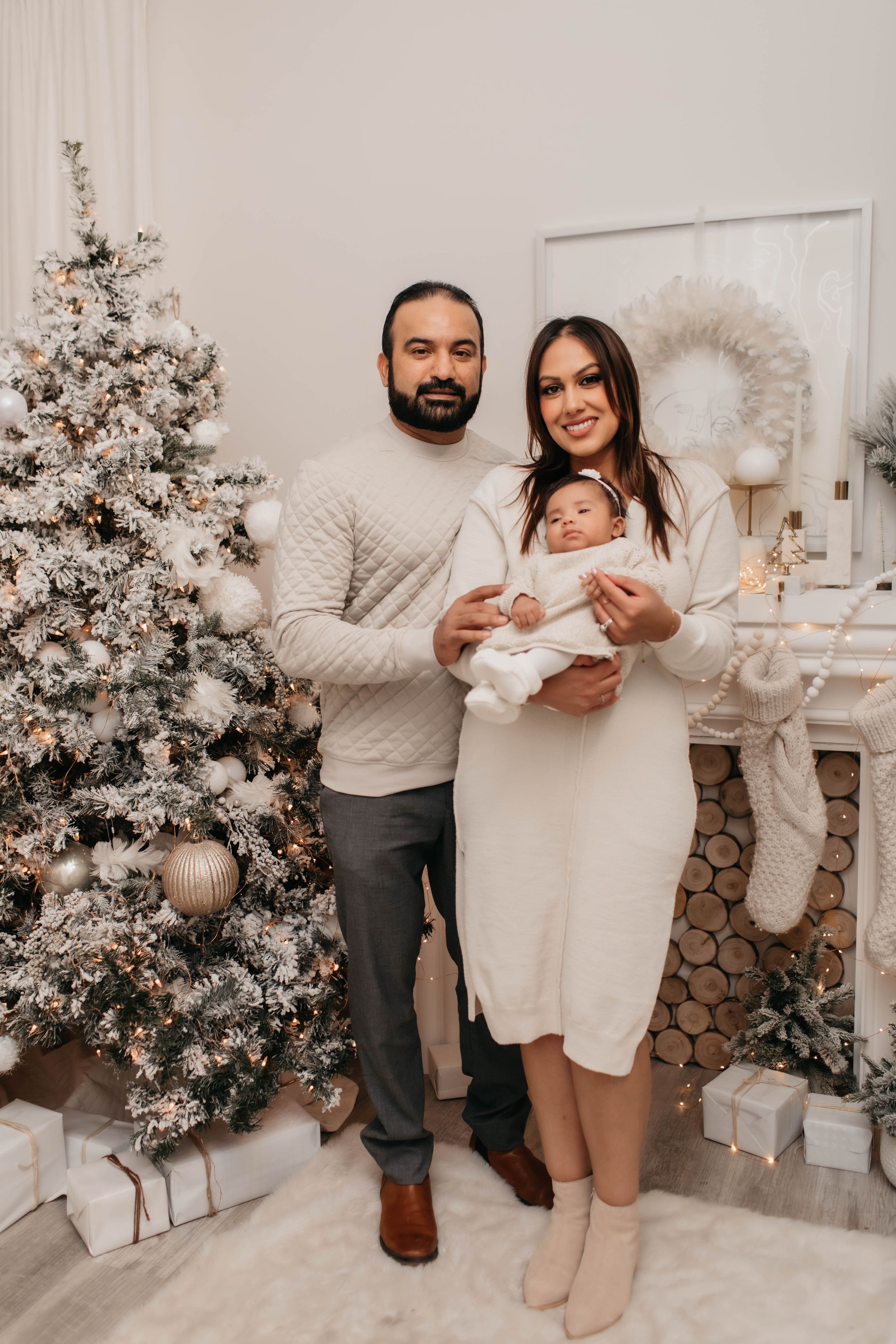 Holiday family portrait by Christmas tree with cream and white decor and wooden fireplace accent.