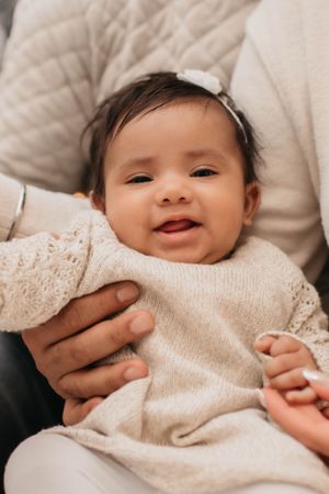 Smiling baby wearing white bow and cream sweater in close-up portrait.
