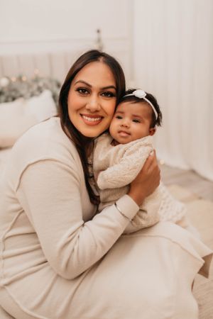 Warm winter portrait of parent and baby in matching cream outfits with holiday decor.