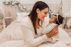 Cozy winter scene showing tender moment between parent and infant on white bedding with holiday decorations in background.