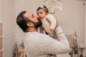 Tender moment between parent and baby in white knit sweater with Christmas decor.