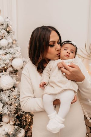 Intimate holiday portrait with cream sweaters against decorated Christmas tree background.