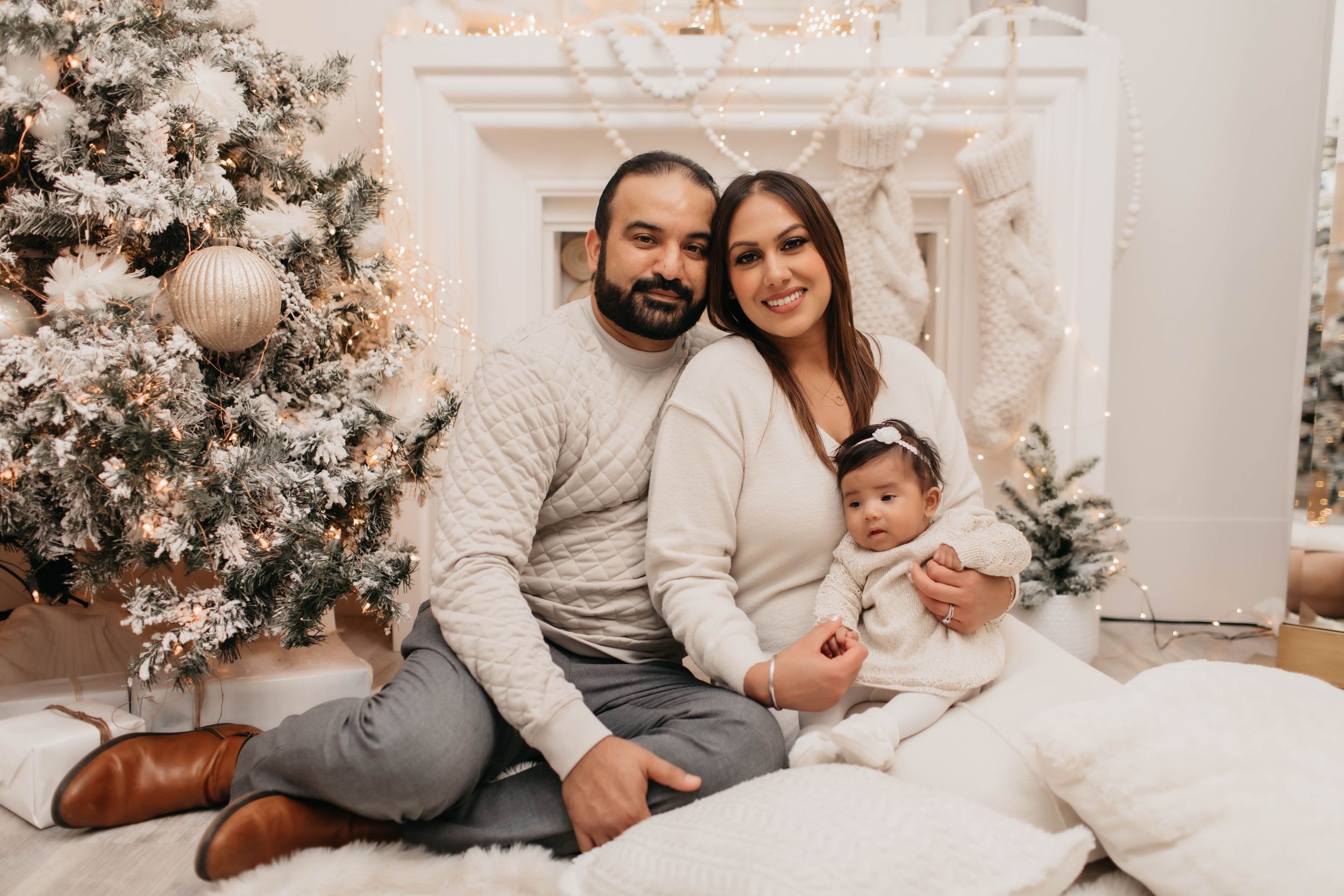 Family Christmas photo with decorated tree and white fireplace in warm neutral colors.