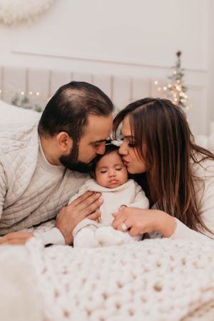 Intimate family moment captured on white bedding with soft winter lighting.